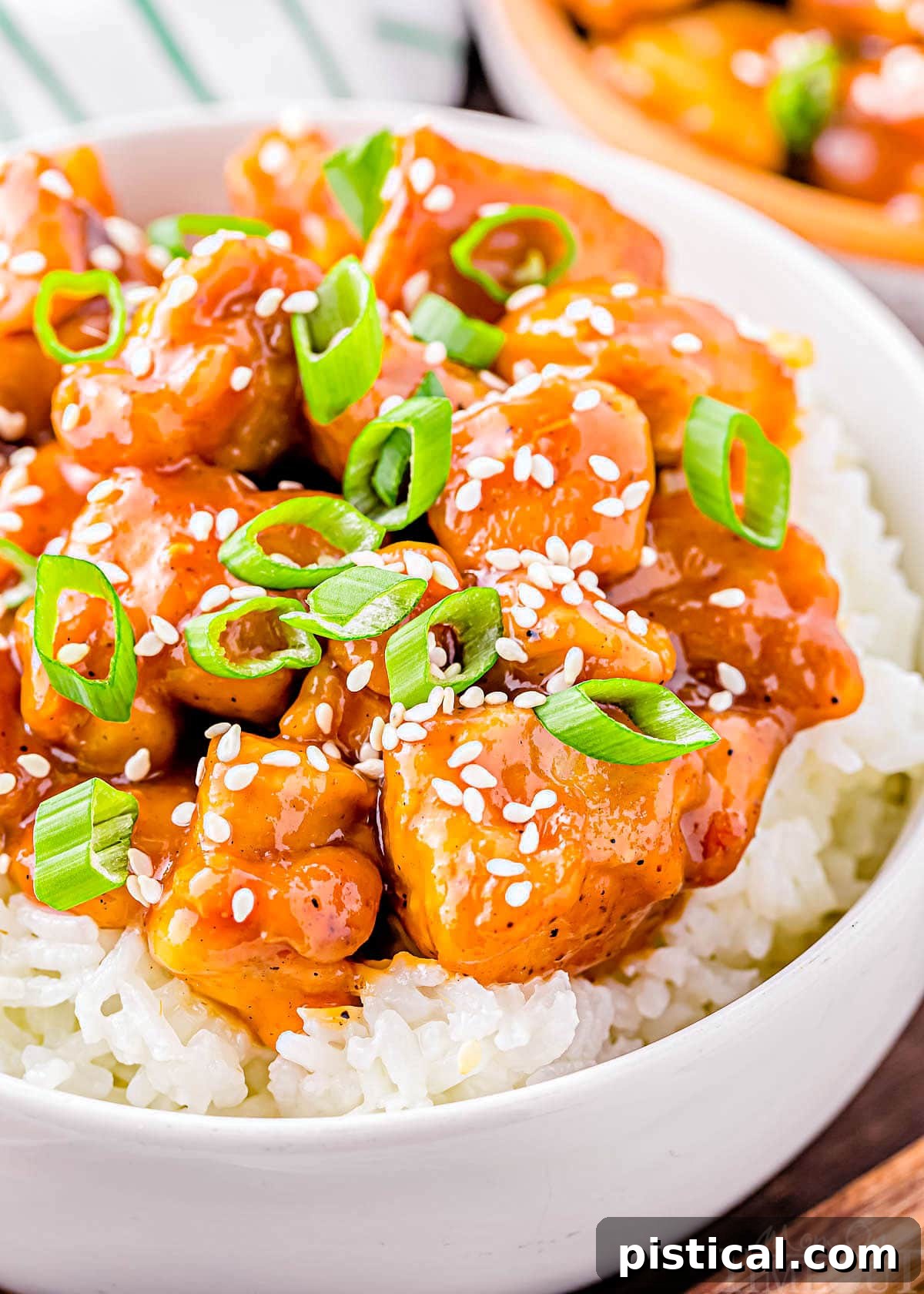 Sticky Honey Garlic Chicken 5 close up look at honey garlic chicken in white bowl with white rice. chicken is garnished with sliced green onions and white sesame seeds.