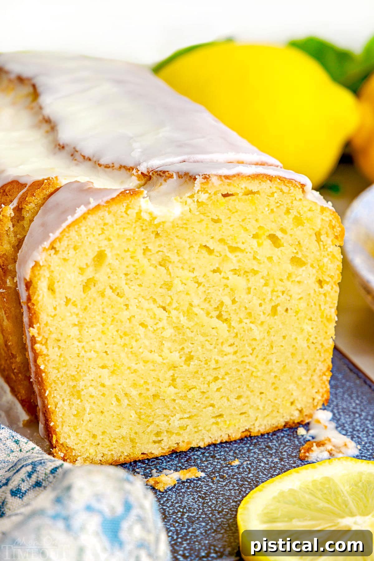 loaf of lemon limoncello cake with limoncello glaze sitting on a blue speckled ceramic board. A few slices have been cut off so you are seeing the crosssection.