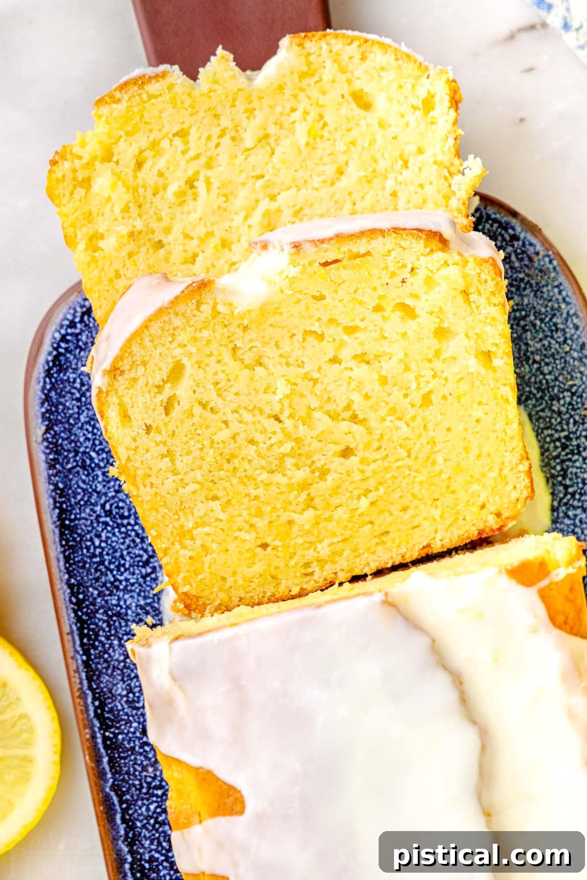top down look at two slices of limoncello cake  and the rest of the loaf cake on a blue glazed clay cutting board.