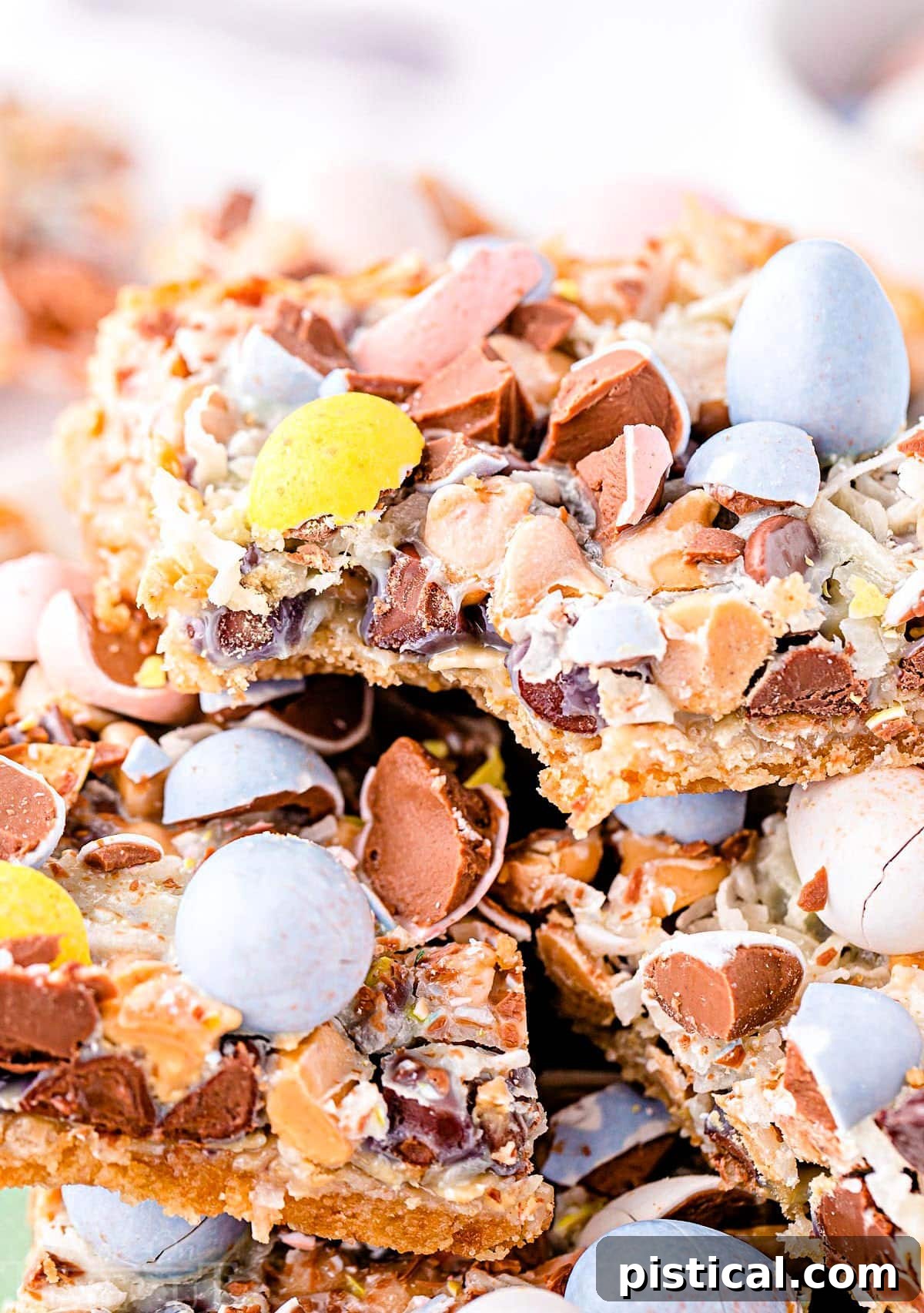 cadbury eggs seven layer bars stacked on a plate with the top bar having a bite taken.