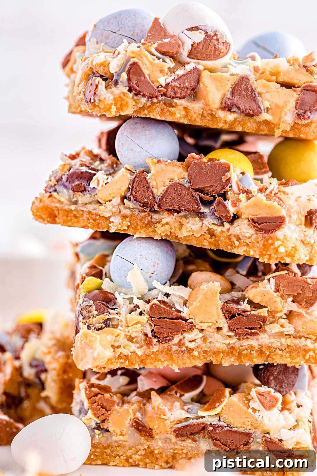 close up look at magic cookie bars topped with cadbury easter eggs stacked four high on a white surface.