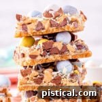 magic cookie bars topped with cadbury easter eggs stacked four high on a white surface.