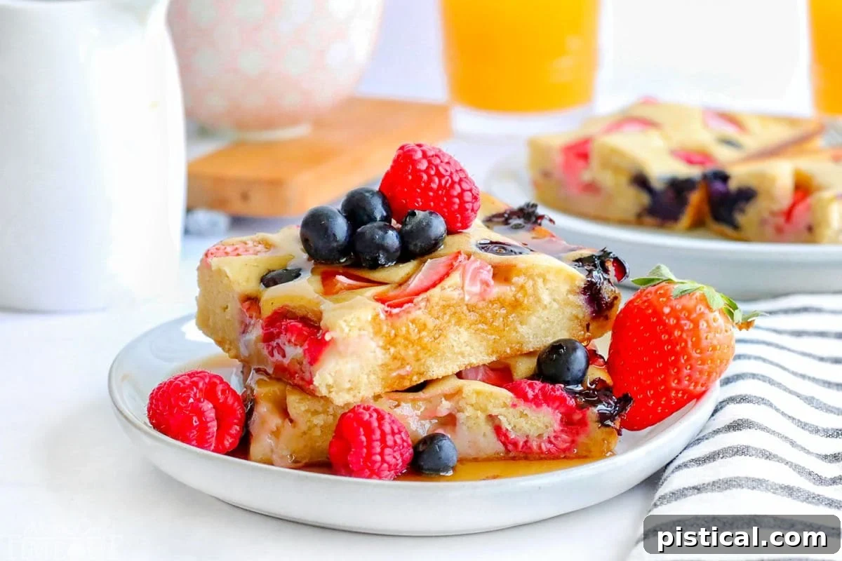 Two square-cut sheet pan pancakes elegantly stacked on a pristine white plate, adorned with a vibrant medley of fresh berries and glistening maple syrup.