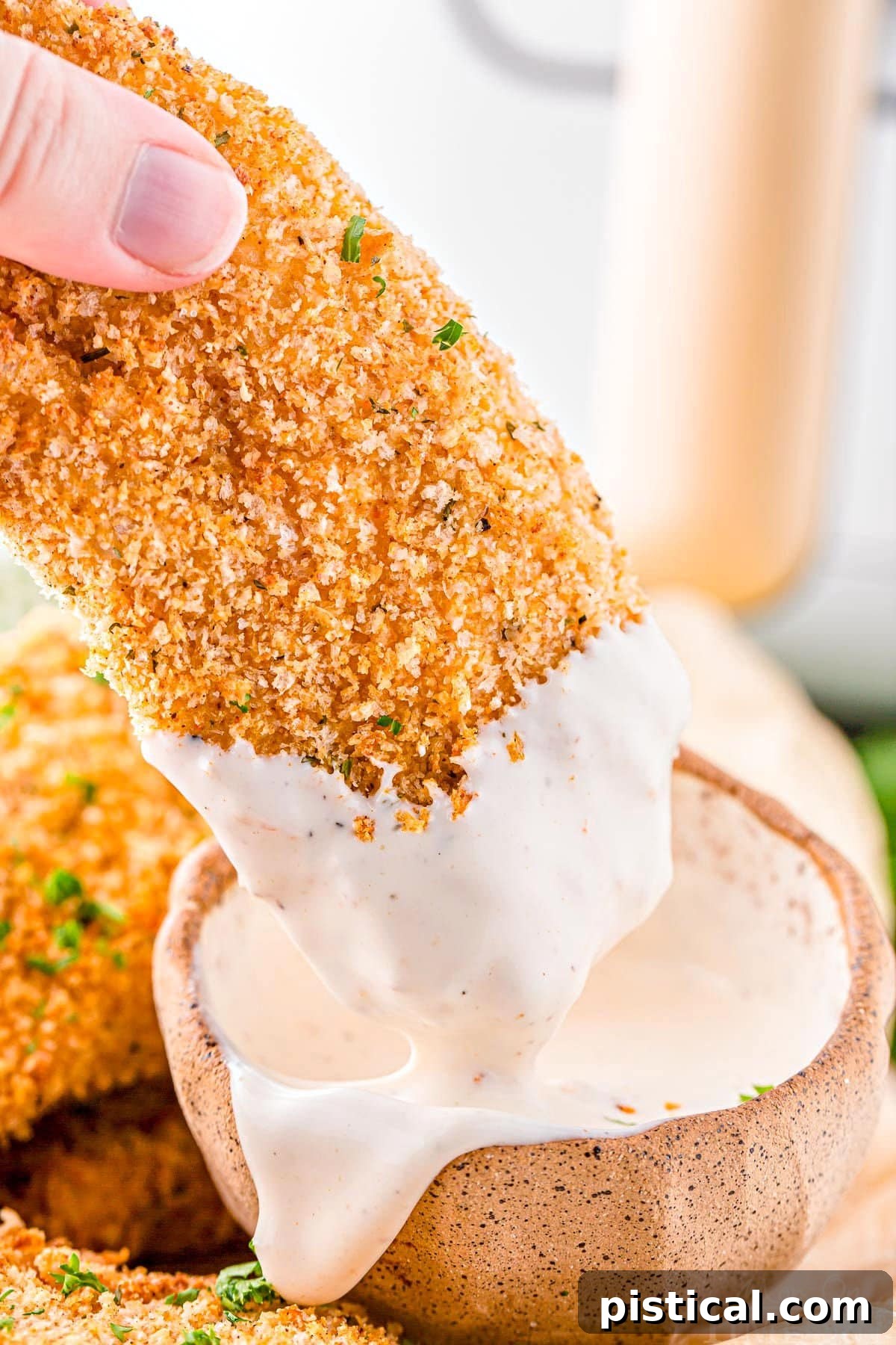 Crispy air fryer chicken tender being dipped into a small bowl of creamy fry sauce.