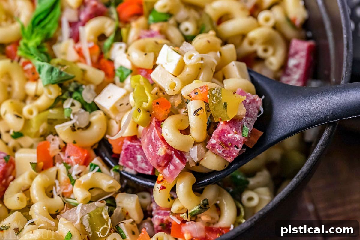 A close-up shot of a serving spoon perfectly capturing a generous scoop of the vibrant Italian pasta salad. The salad is a delightful mix of pasta, slices of savory salami, crisp dill pickles, and a medley of fresh vegetables, all glistening with the rich Italian dressing, ready to be enjoyed.