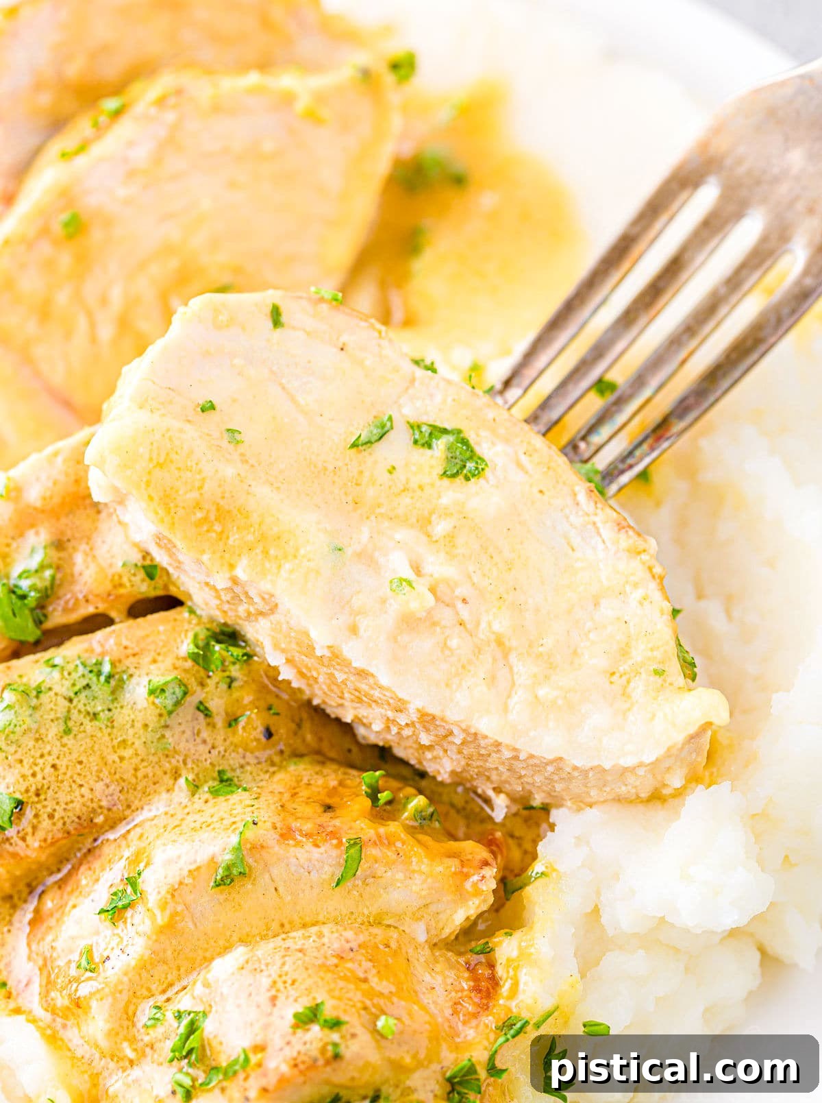 A fork lifting a slice of tender honey mustard chicken breast, coated in its delicious sauce.
