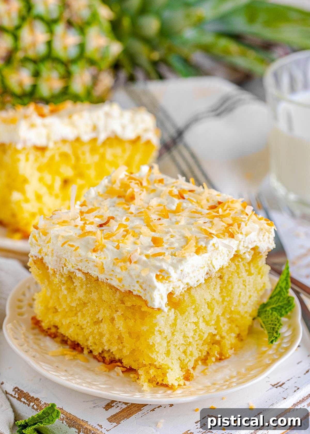 A perfectly portioned single piece of Pina Colada Poke Cake on a crisp white plate, elegantly topped with fluffy pineapple coconut frosting and a sprinkle of toasted shredded coconut, ready to be savored.