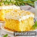 A square slice of moist Pina Colada Cake on a white plate, generously frosted with fluffy white coconut frosting and garnished with golden toasted coconut flakes.