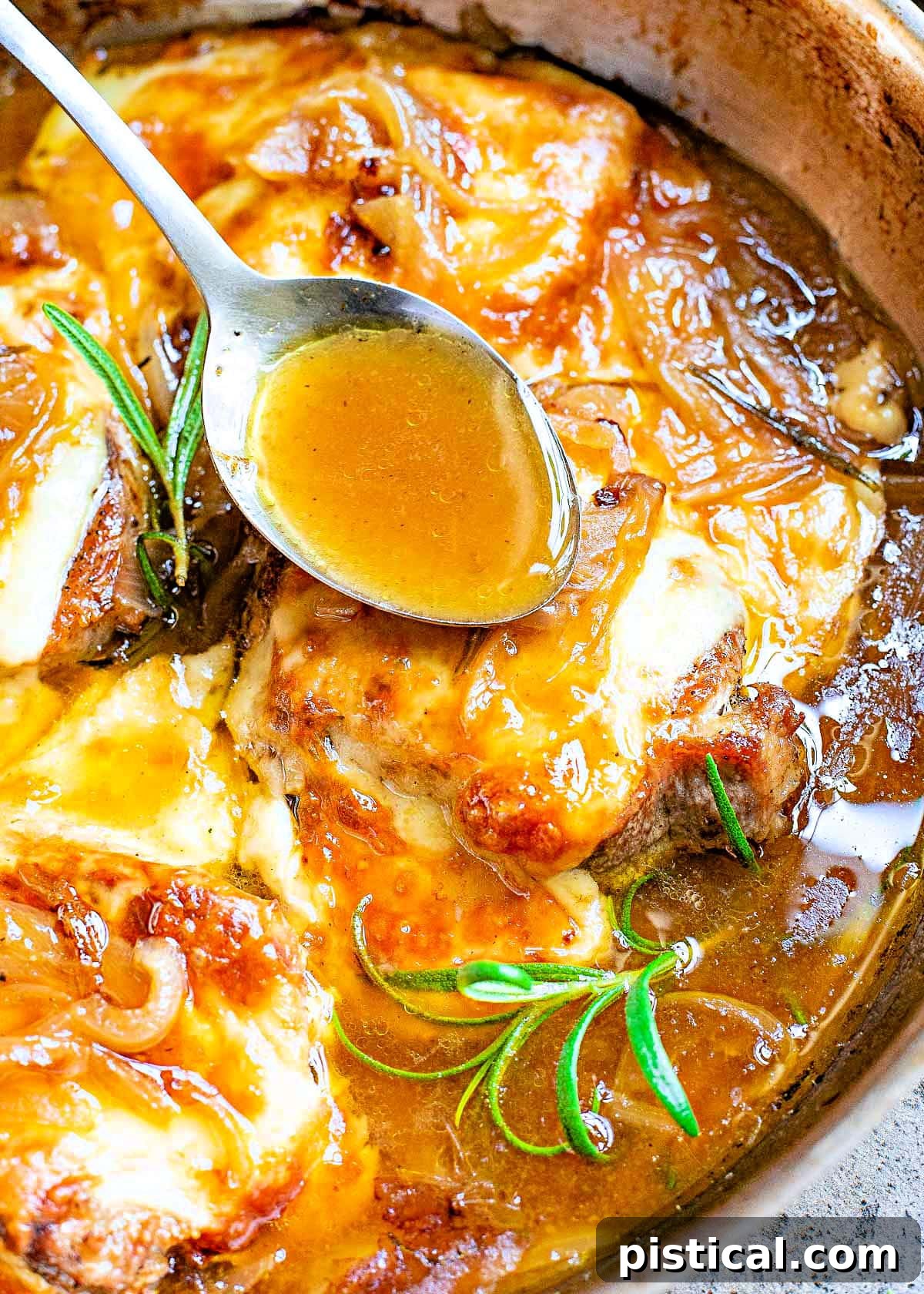 spoonful of sauce being drizzled over browned cheese on top of french onion pork chops in a large skillet.