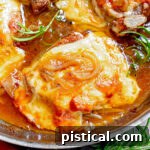 close up look at french onion pork chops in a stainless steel skillet topped with melted and browned cheese. fresh rosemary sprigs are scattered about.