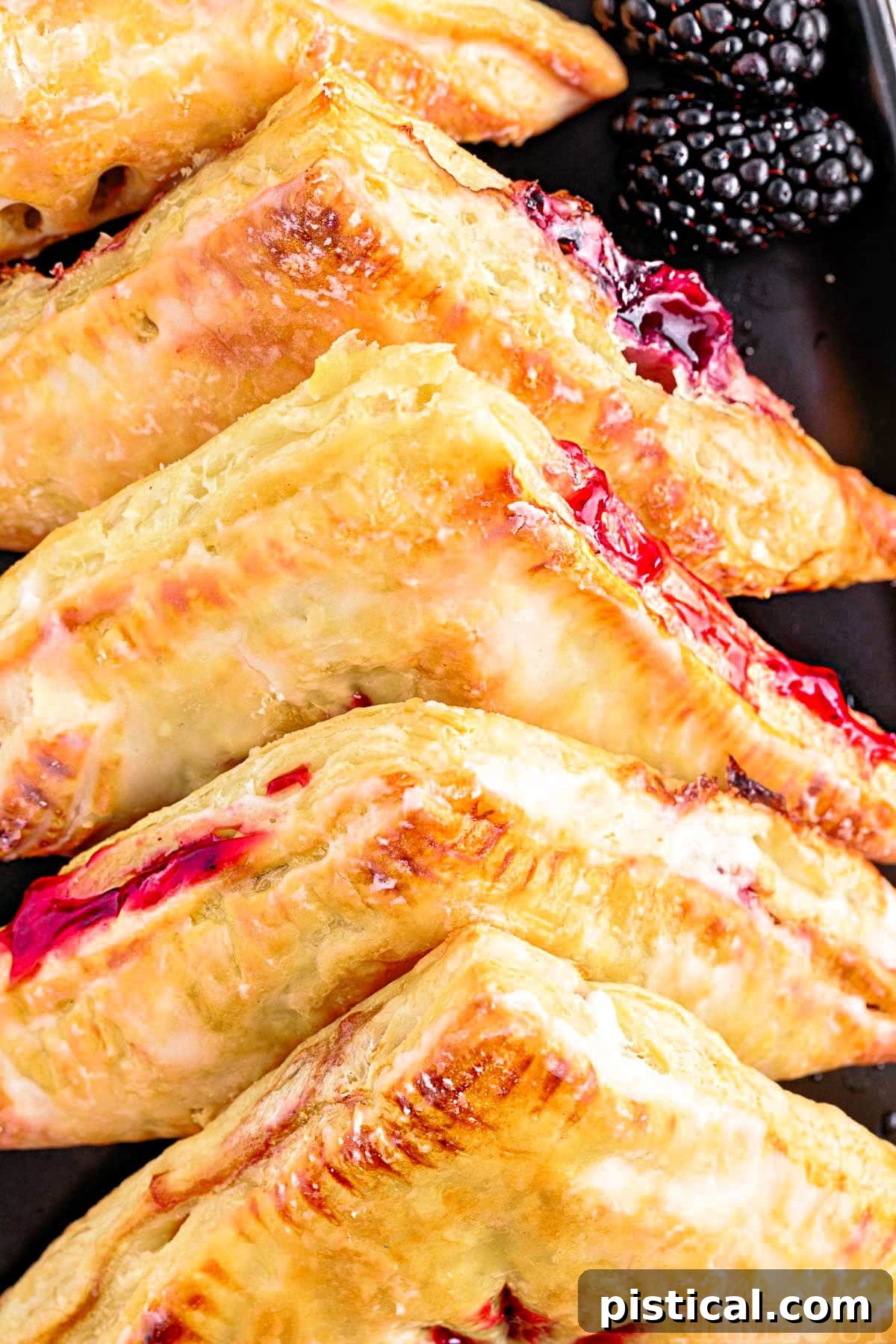 Close-up view of blackberry turnovers on a black plate, showcasing the rich, dark fruit filling peeking through the flaky pastry.