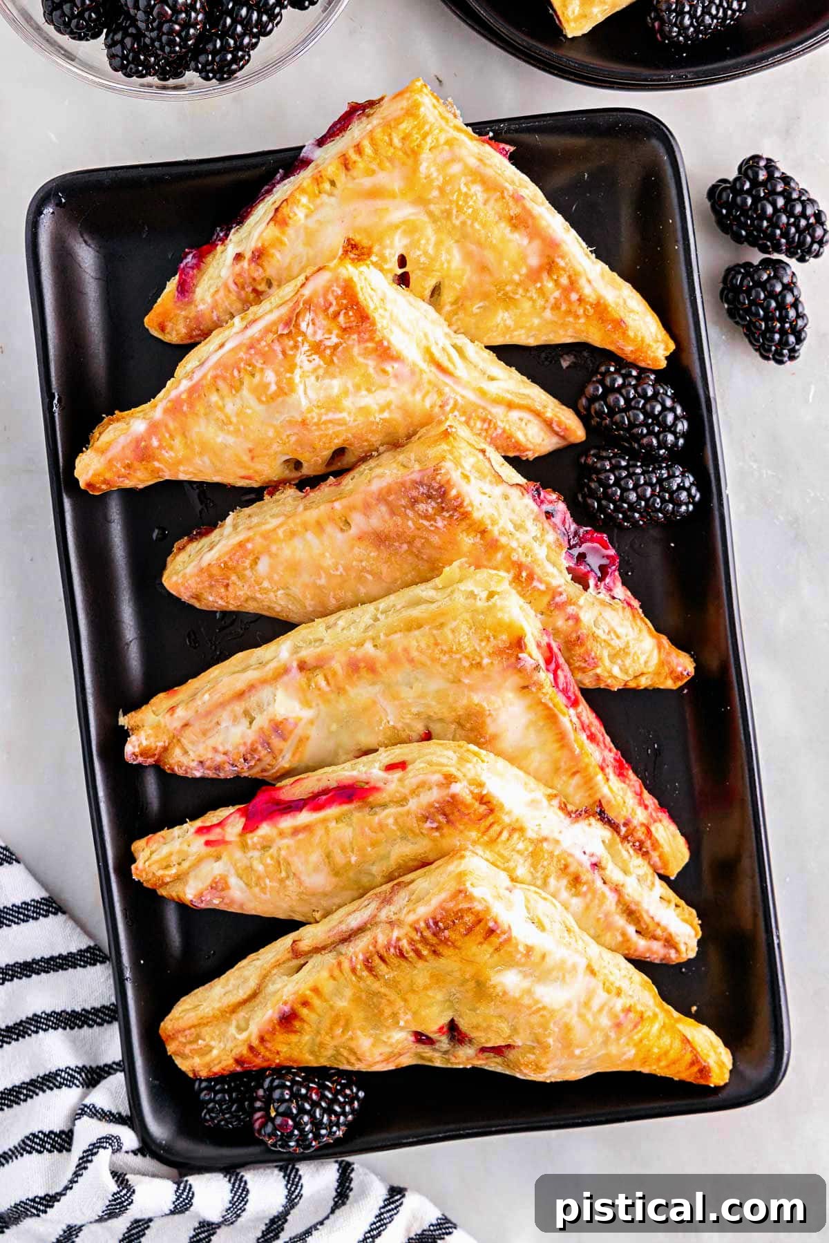 Top-down view of perfectly glazed blackberry turnovers arranged on a black rectangular plate, ready to be served.