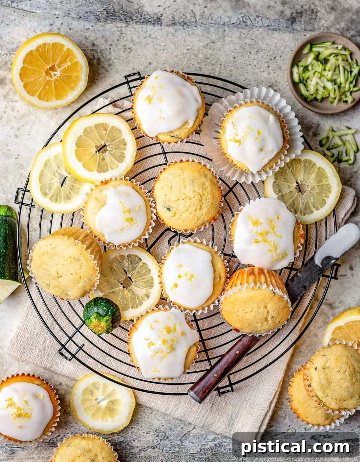 Zesty Lemon Zucchini Muffins 3 top down look at glazed zucchini muffins made with lemon on a black wire cooling rack with slices of lemon scattered about.