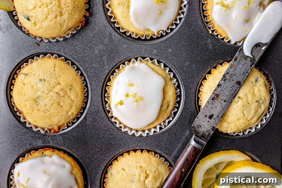 Zesty Lemon Zucchini Muffins 5 lemon zucchini muffins in muffin tin with half of them glazed and the glaze knife resting across the top of the pan.