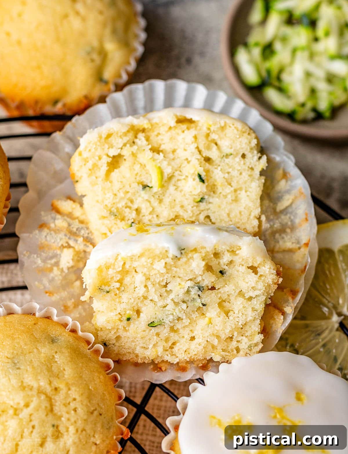 Zesty Lemon Zucchini Muffins 6 lemon zucchini muffin cut in half with one half resting on the other. three whole muffins and some shredded zucchini are near the cut muffin.