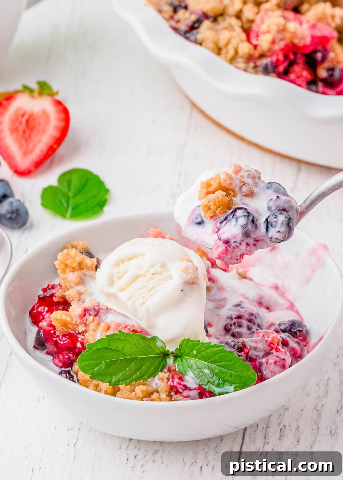 A pristine white bowl showcasing a warm, rich berry cobbler, beautifully topped with a generous scoop of melting vanilla ice cream. A spoon is mid-scoop, capturing the delicious, bubbling fruit and soft topping.