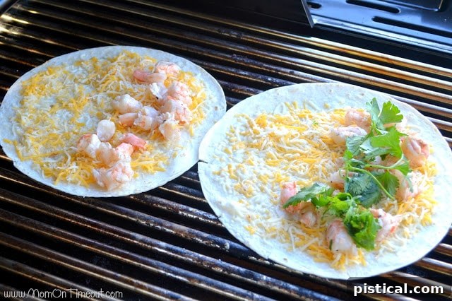 A quesadilla being folded in half on the grill, showing melted cheese and fillings