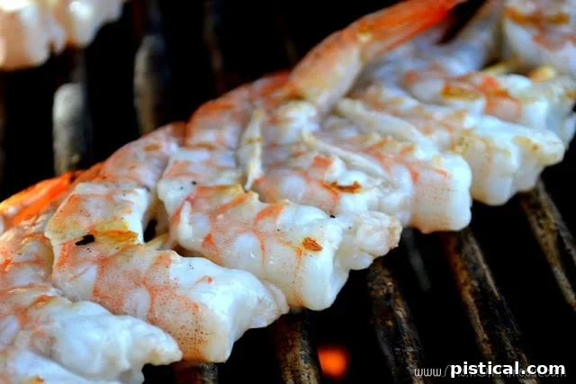 Perfectly grilled shrimp skewers being removed from the grill with tongs