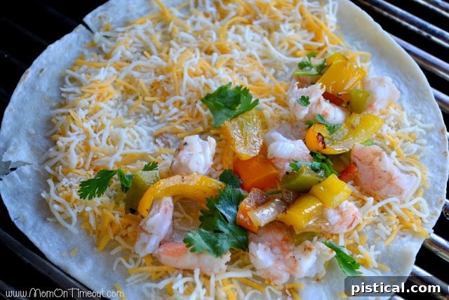 A tortilla with cheese, shrimp, and cilantro placed on one half, on the grill