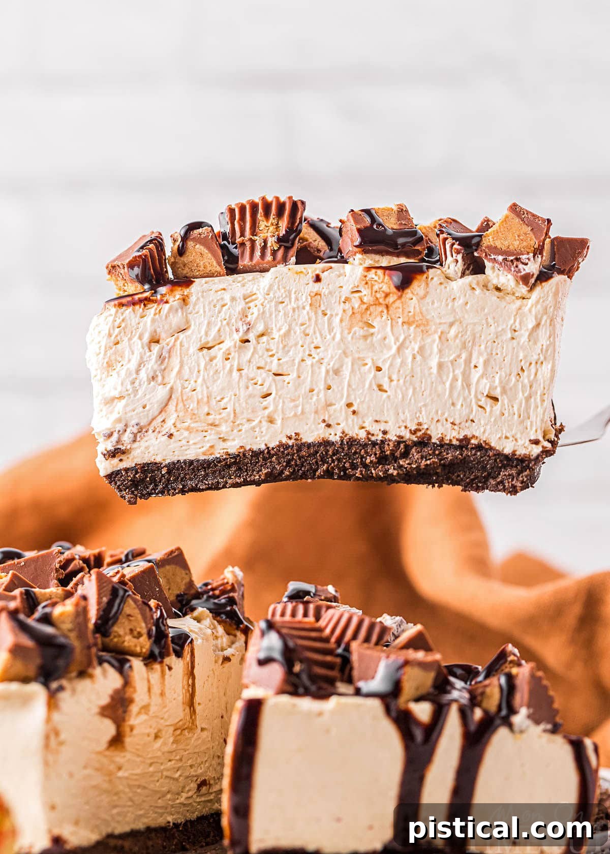A slice of creamy peanut butter cheesecake is held aloft, showing its layers, before being placed onto a plate next to the remaining cheesecake still in the pan.