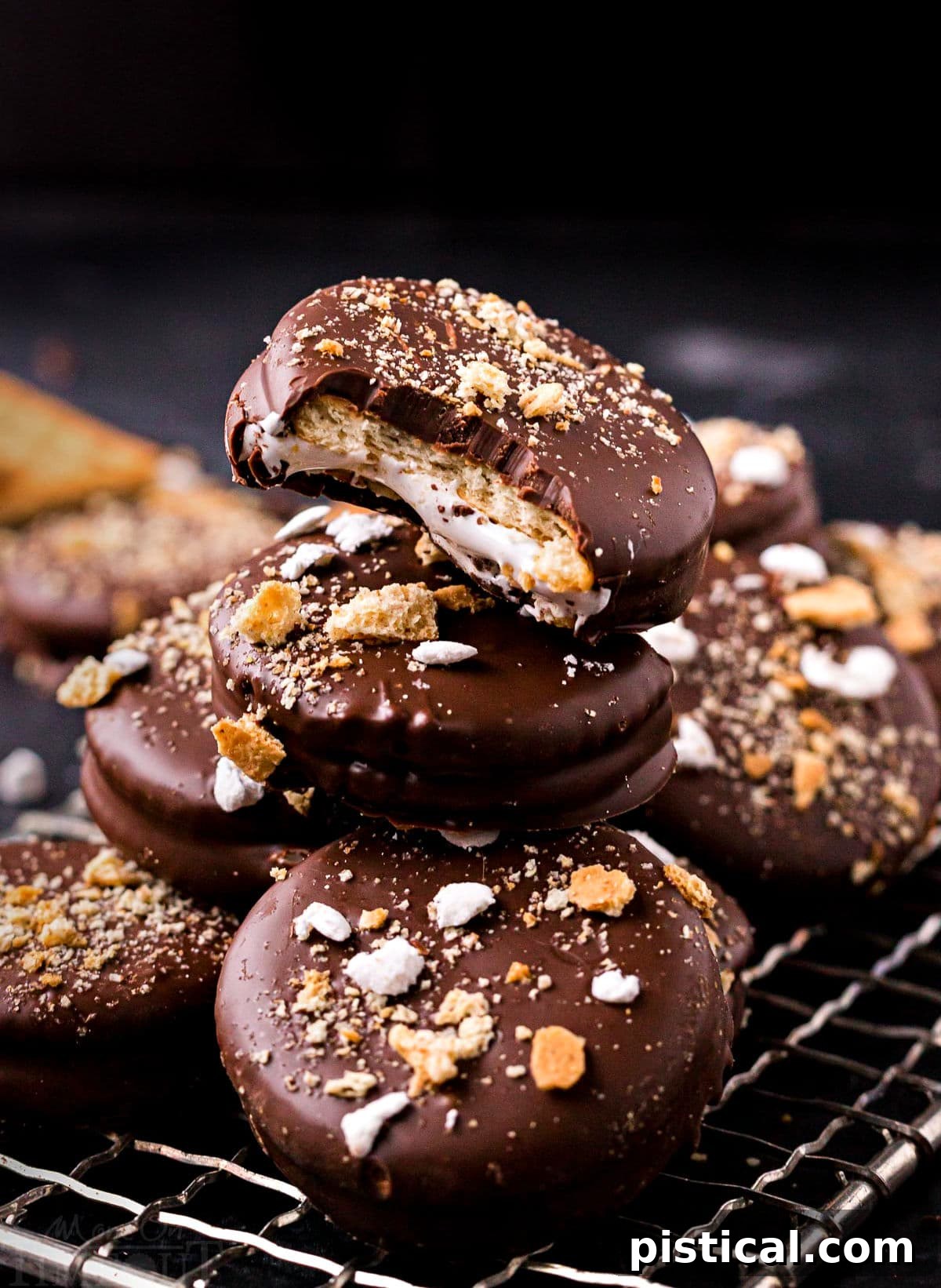 Delightful no-bake Ritz cracker s'mores cookies with marshmallow filling, dipped in chocolate, and topped with crushed graham crackers and mini marshmallows, stacked on a small wire rack.