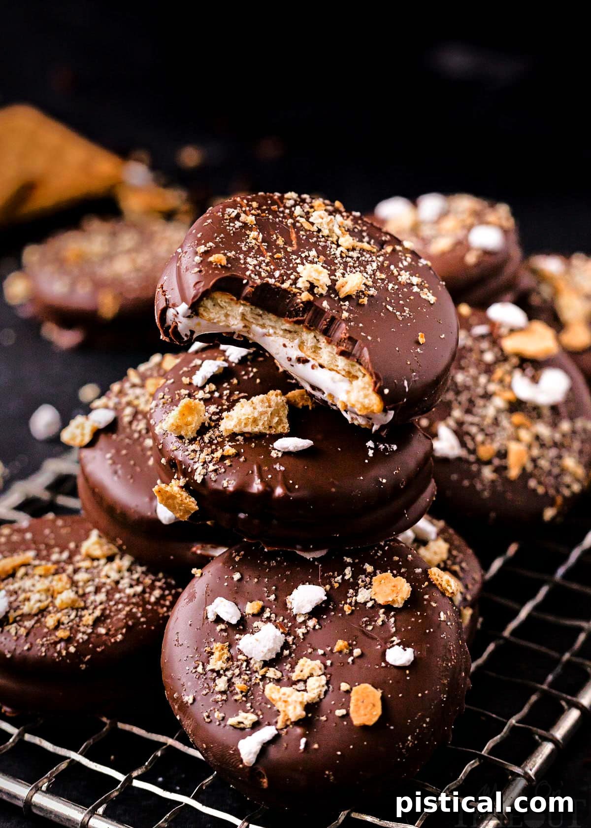 No-bake Ritz cracker sandwich cookies with marshmallow filling and dipped in chocolate, beautifully stacked on a small wire rack. The cookies are generously topped with crushed graham crackers and miniature marshmallows.