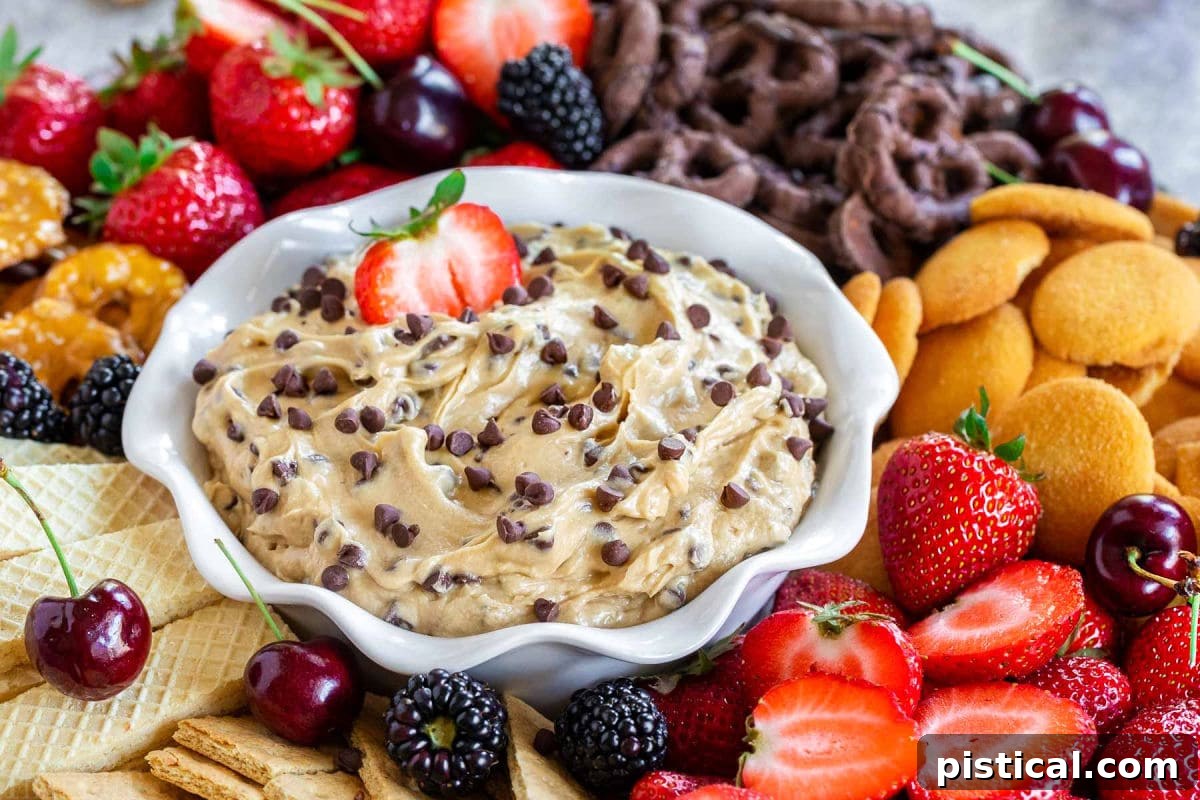A vibrant front view of a white serving bowl, brimming with decadent chocolate chip cookie dough dip. The bowl is artfully encircled by a delicious array of dippers, including various cookies, crisp apple slices, and sweet strawberries, inviting guests to dive in.