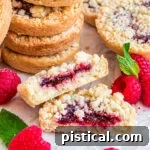 stack of costco raspberry crumble cookies with one cookie broken in half laying in front next to fresh raspberries.