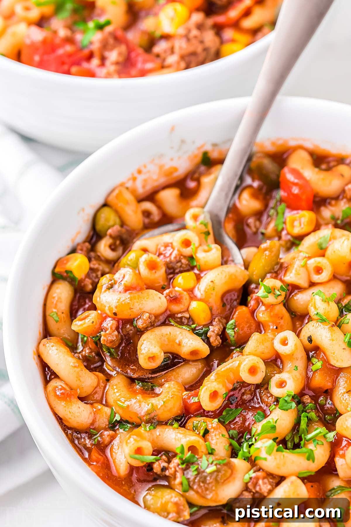 Homestyle Beef Macaroni Soup 6 A full bowl of Hamburger Macaroni Soup with a spoon dipped in, ready to scoop out a bite of the rich, comforting meal, garnished with fresh herbs.