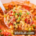 Ladle full of macaroni soup held above a white Dutch oven full of Hamburger Macaroni Soup.
