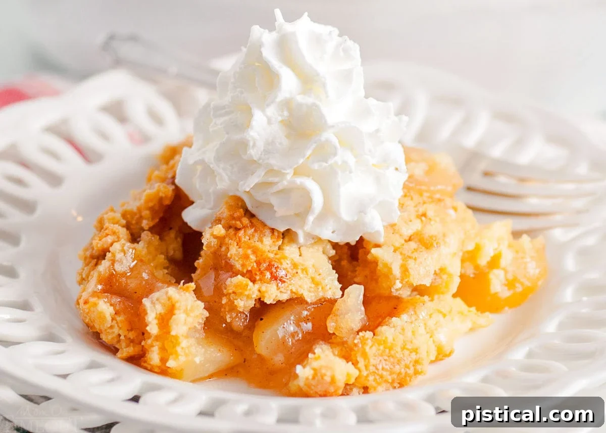 Golden Apple Cobbler Delight 7 scoop of apple cobbler served on a white lace edged plate topped with fresh whipped cream. white casserole dish with remaining cobbler in the background.