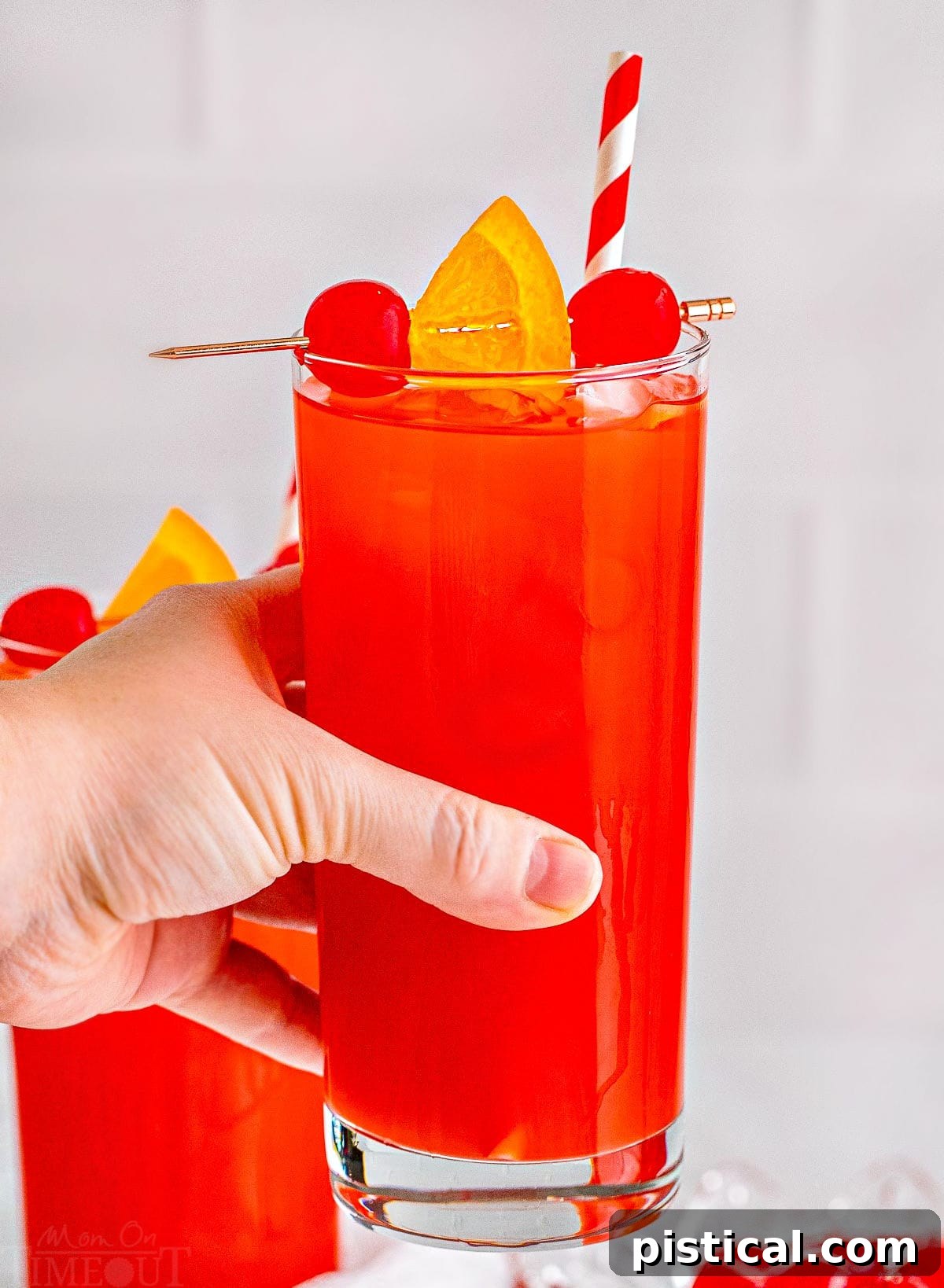 An Alabama Slammer cocktail, beautifully garnished with a maraschino cherry and an orange slice, held aloft with a festive red and white striped straw.