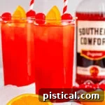 Two tall glasses filled with a vibrant Alabama Slammer cocktail, adorned with red and white striped straws. A bottle of Southern Comfort and a halved orange are visible in the background.