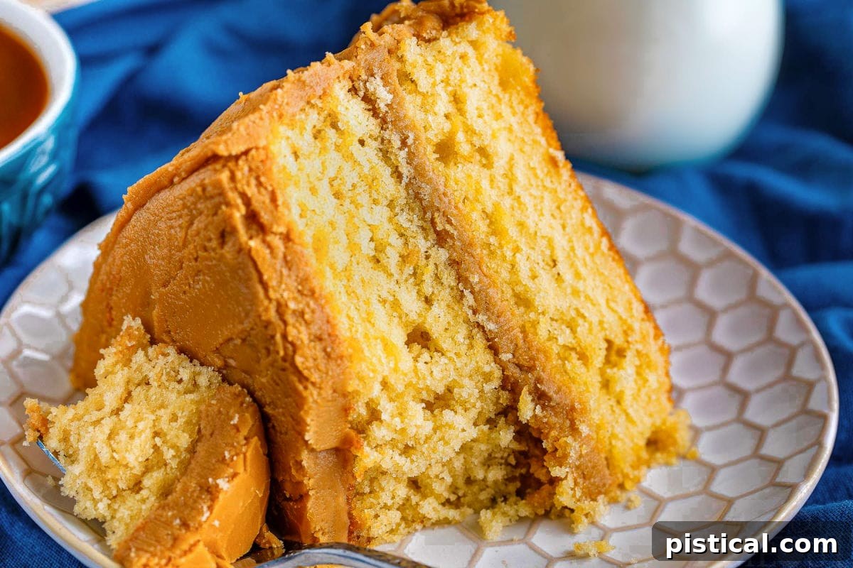 A delectable slice of caramel layer cake is presented on a white plate, with a fork holding a small piece of cake resting on the side, highlighting the moist texture and glossy frosting.