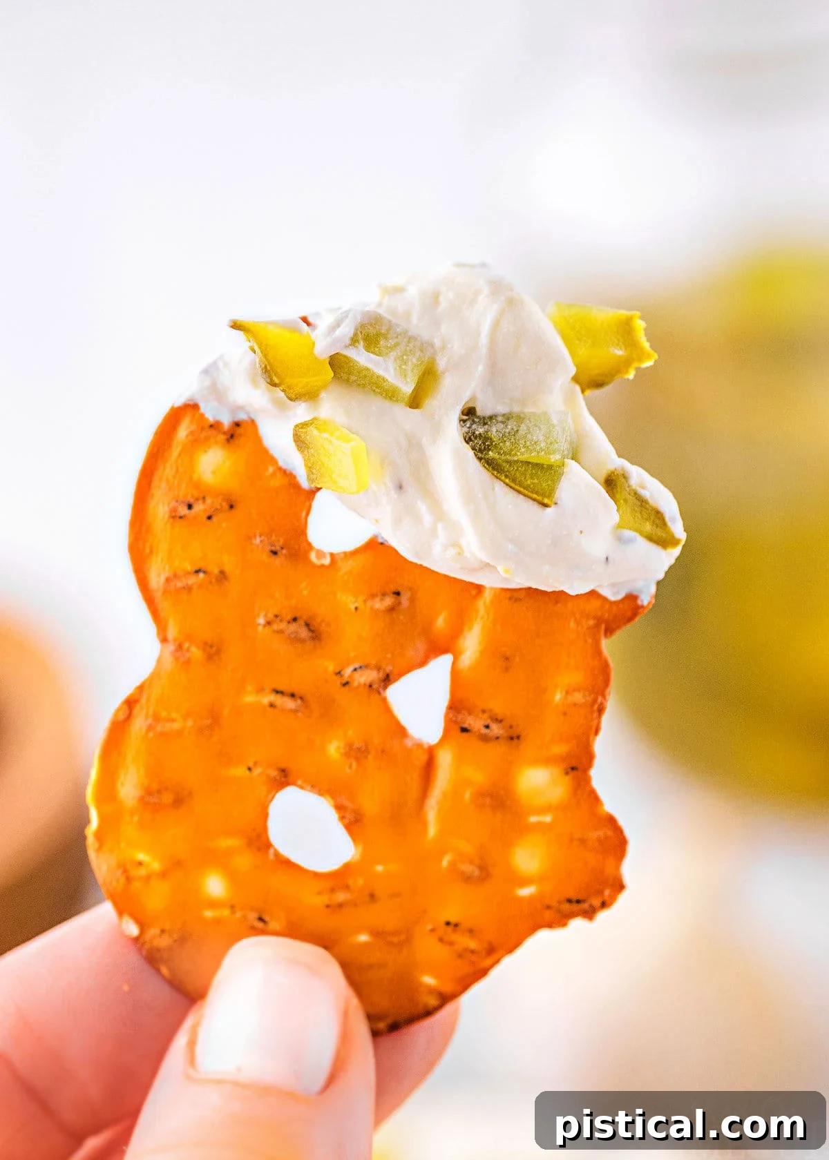 Dillicious Dip 3 A pretzel chip is held up, coated with a generous dollop of creamy dill pickle dip on its end.