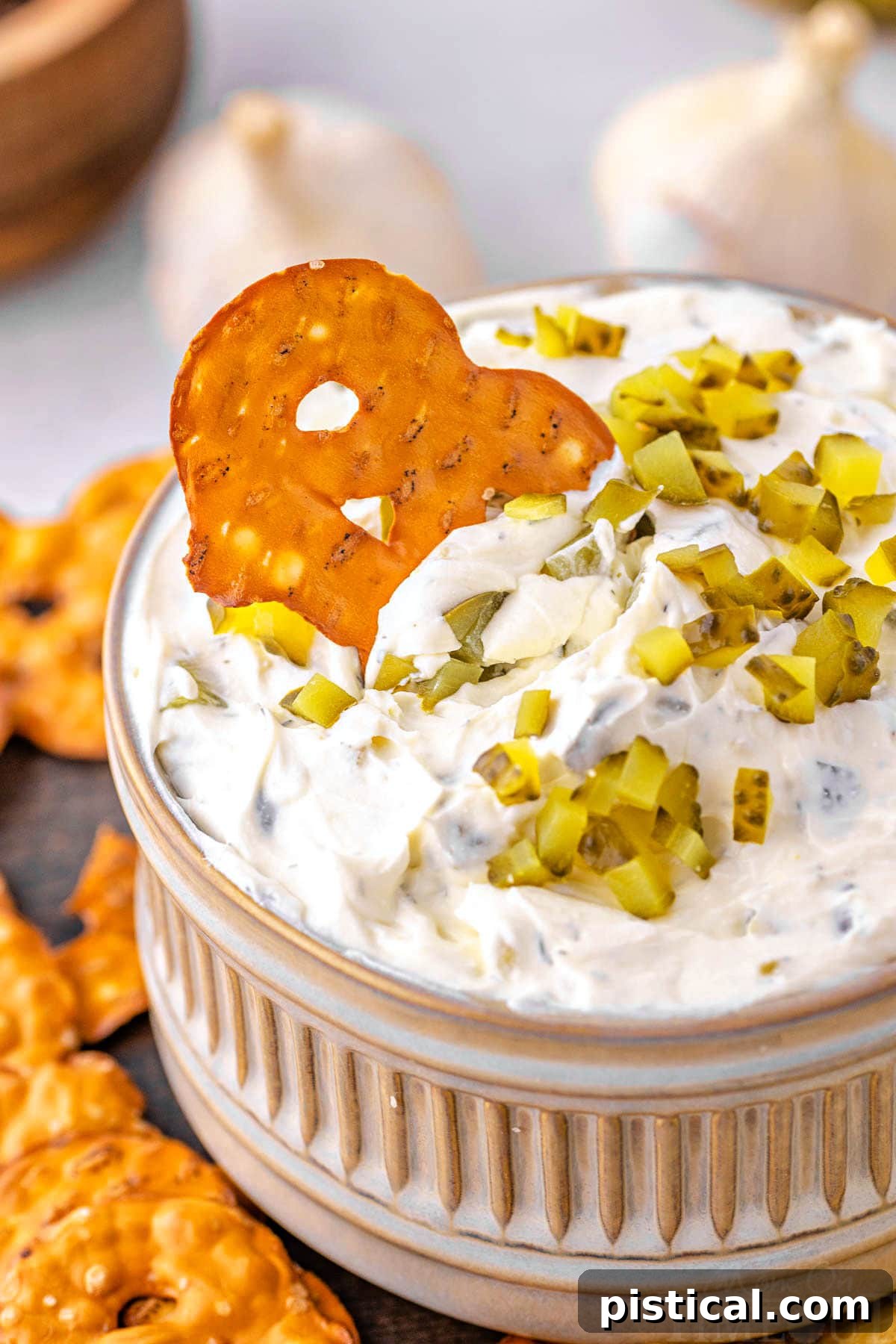 Dillicious Dip 7 A pretzel chip is being dipped into a small, elegant bowl generously filled with creamy dill pickle dip.