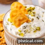 Dillicious Dip 8 small clay bowl with dill pickle dip in it. three crackers are dipped into the dip with a sprinkle of chopped pickle scattered on top.