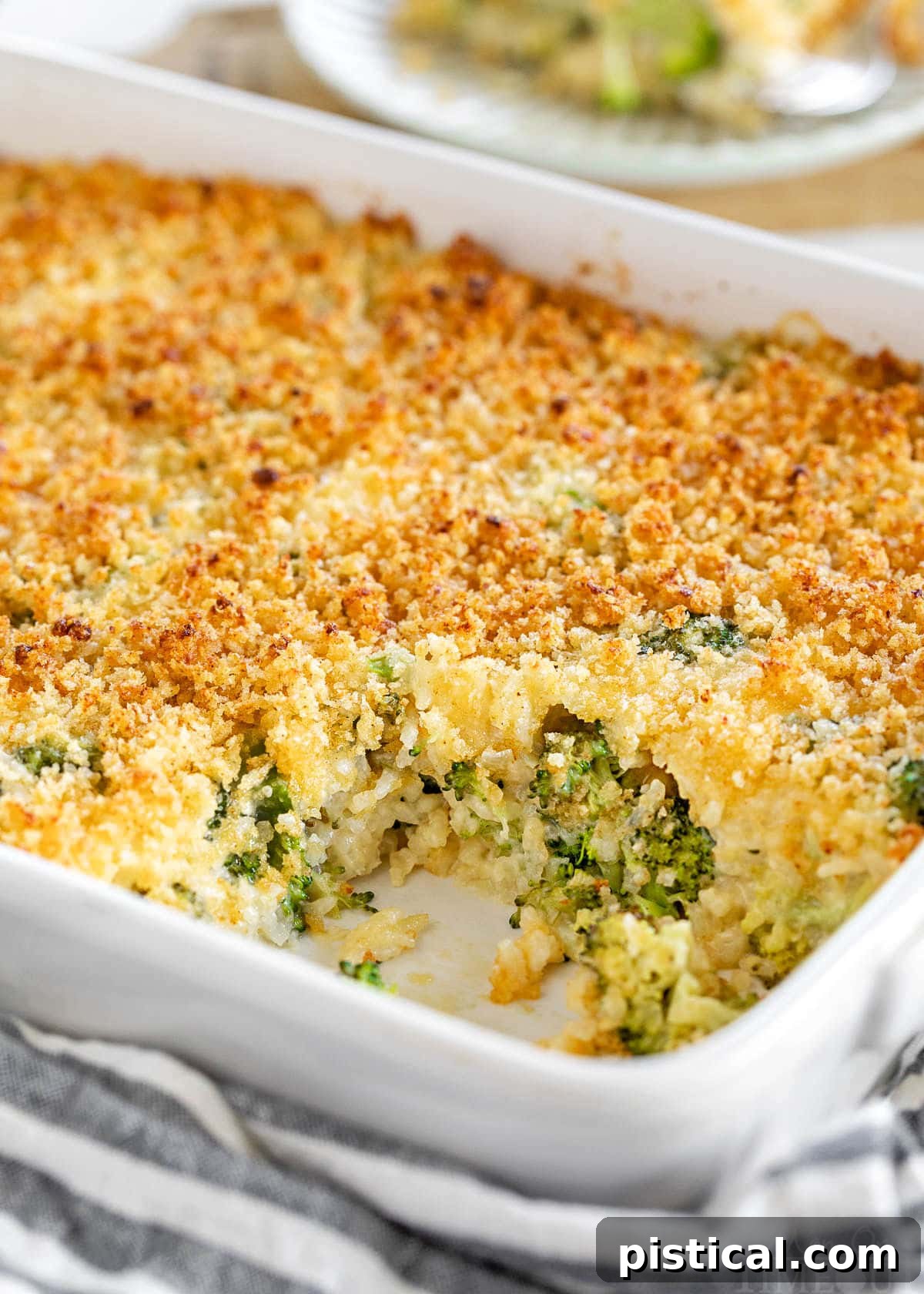 white casserole dish with broccoli rice casserole recipe in it. scoop of the casserole has been removed and is on a small white plate in the background.