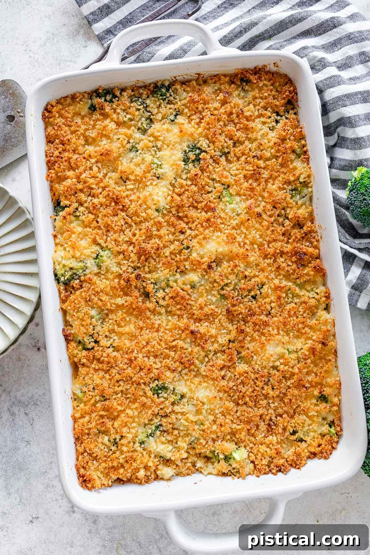 top down look at broccoli rice cheese casserole in a white baking dish next to a black and white striped towel.