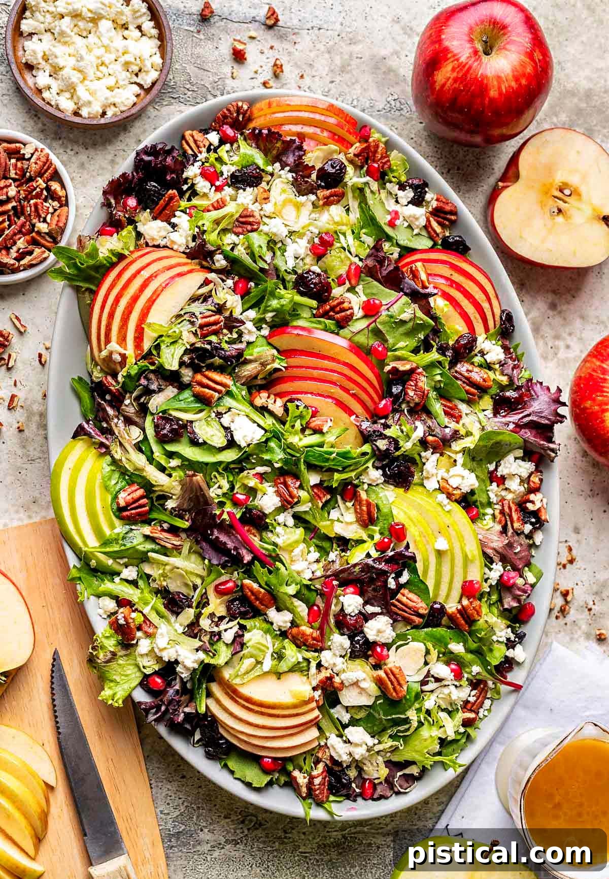Crisp Autumn Apple Salad 2 top down look at apple salad made with brussels sprout, apples, cranberries and topped with a vinaigrette. oval serving bowl is sitting on a gray surface with cut apples around it.