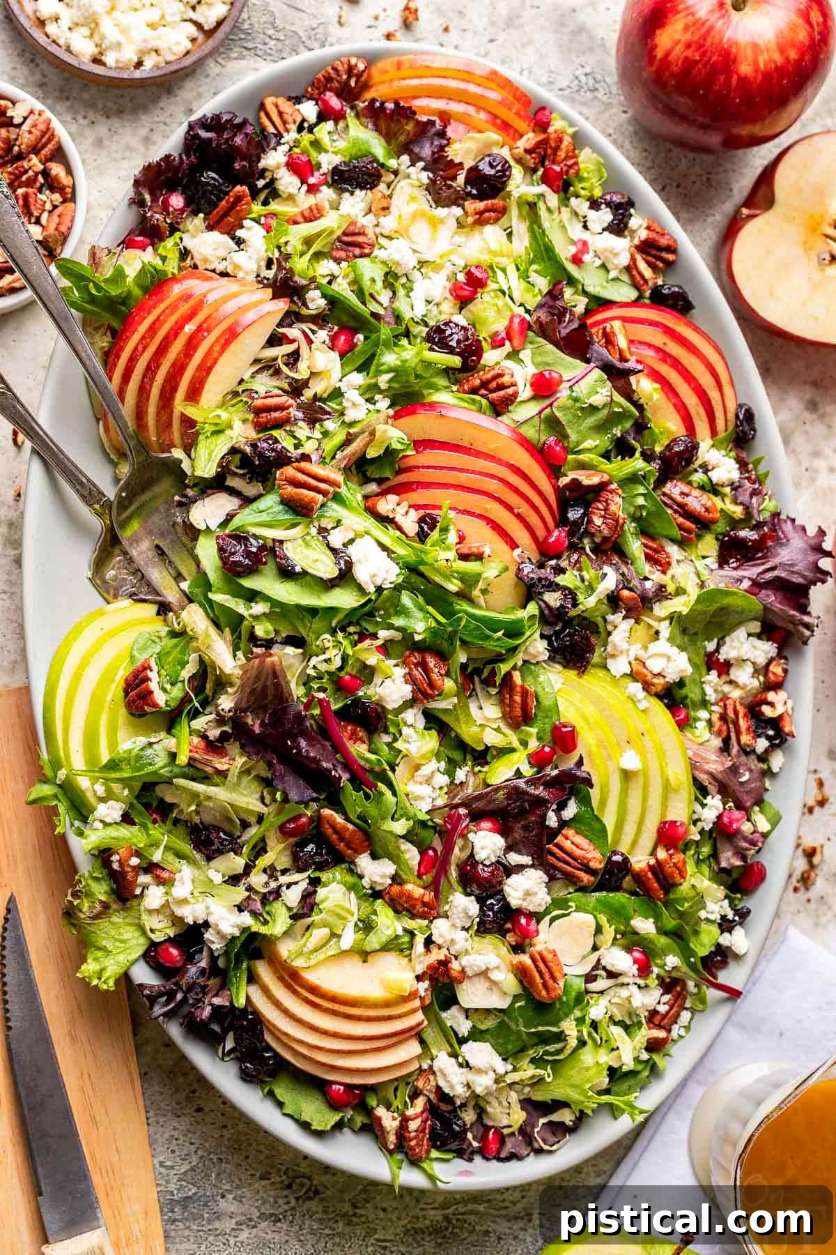 Crisp Autumn Apple Salad 8 top down look at apple salad made with brussels sprout, apples, cranberries and topped with a vinaigrette. oval serving bowl is sitting on a gray surface with cut apples around it.