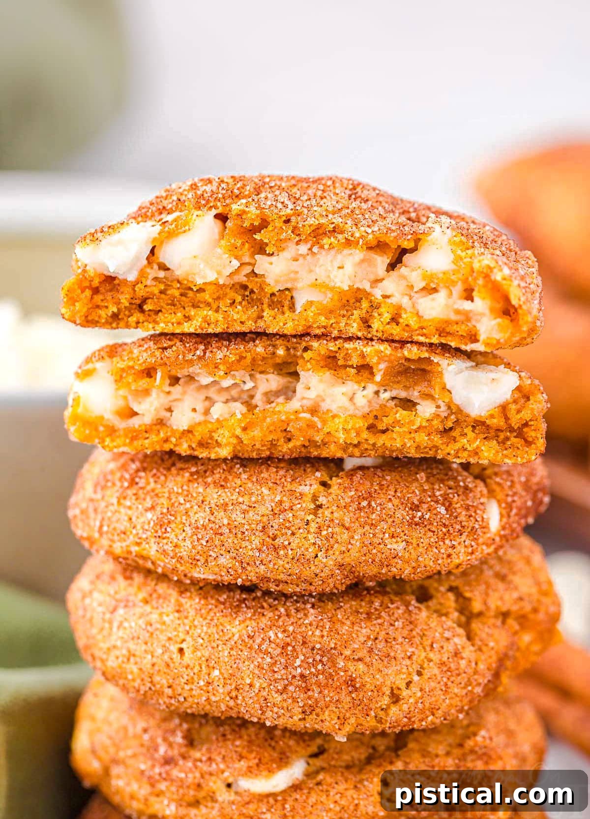 Pumpkin snickerdoodle cookies stuffed with cheesecake filling stacked on top of each other, with the top cookie torn in half to reveal the creamy filling.