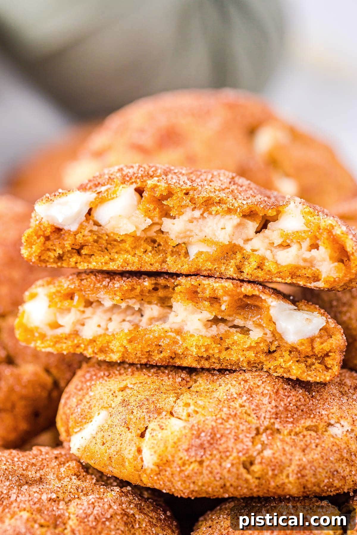Pumpkin snickerdoodle cookies stuffed with cheesecake filling stacked on top of each other, with the top cookie torn in half to reveal the creamy filling.