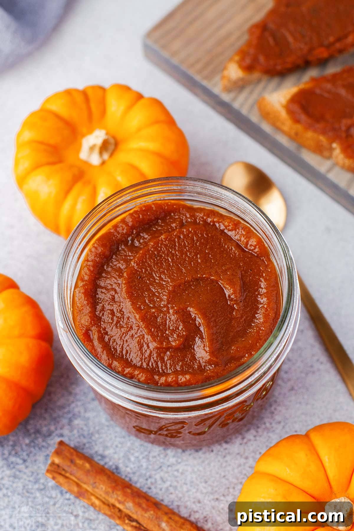 top down look at glass jar filled with pumpkin butter. gold spoon in the pumpkin butter and three small pumpkins surround the jar.