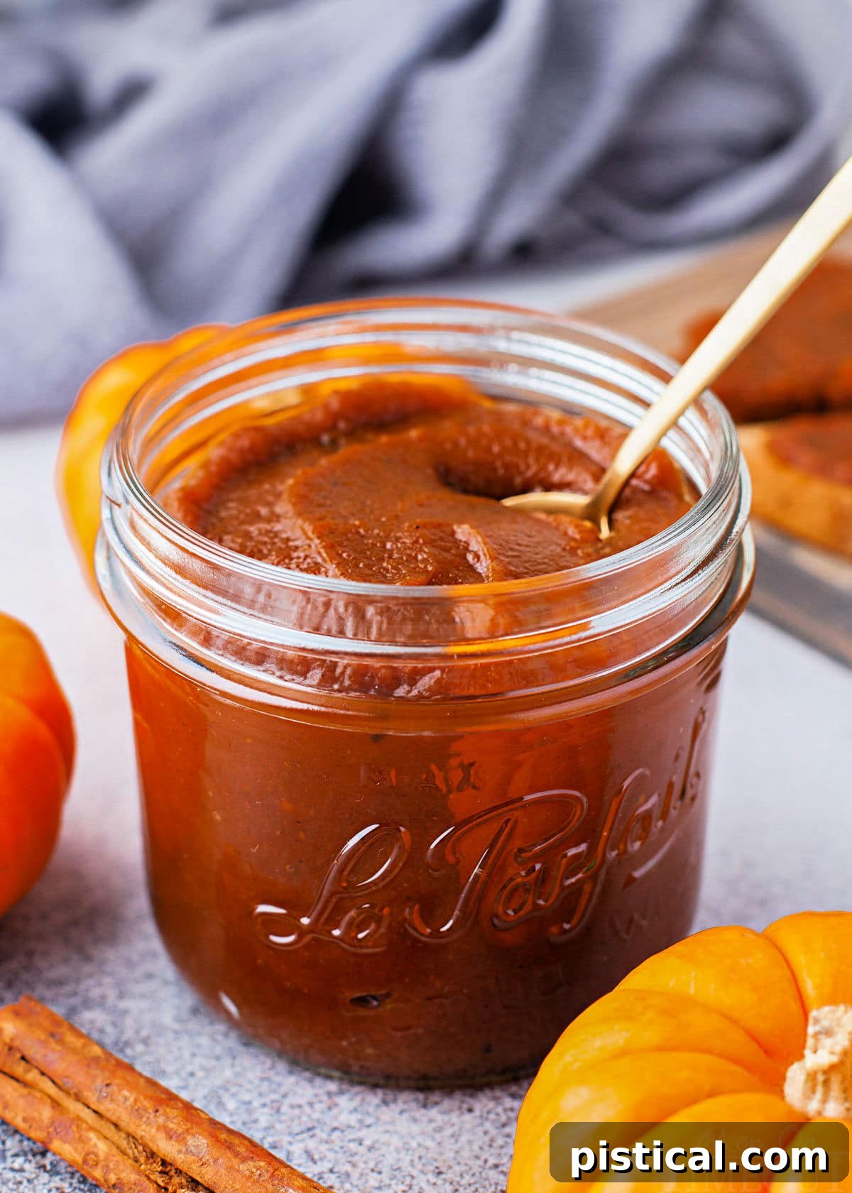 jar of pumpkin butter with small gold spoon sitting in front of a blue napkin. small pumpkin and cinnamon stick are near the jar.