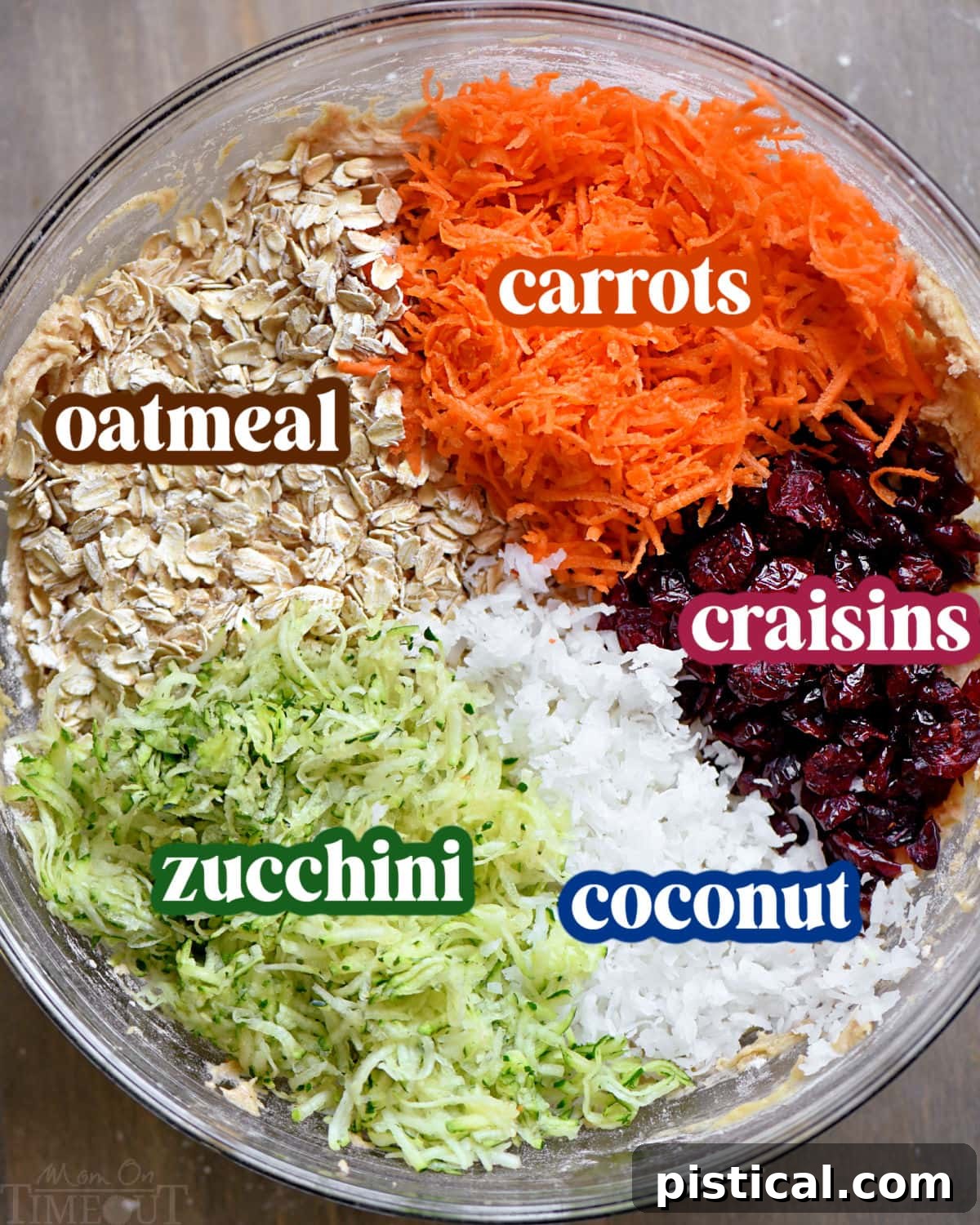 An overhead view of various baking ingredients, including flour, sugars, oats, grated zucchini, carrots, and cranberries, neatly arranged in separate bowls, ready for making zucchini cookies.
