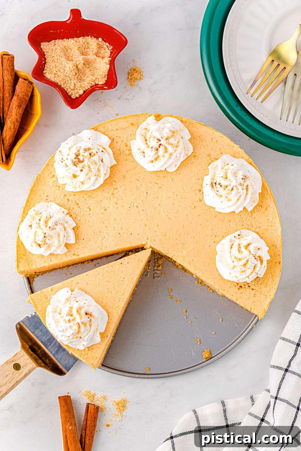 Decadent No Bake Pumpkin Cheesecake 7 A top-down view of a no bake pumpkin cheesecake with whipped cream dollops. One slice has been removed, and another is cut and ready for serving.