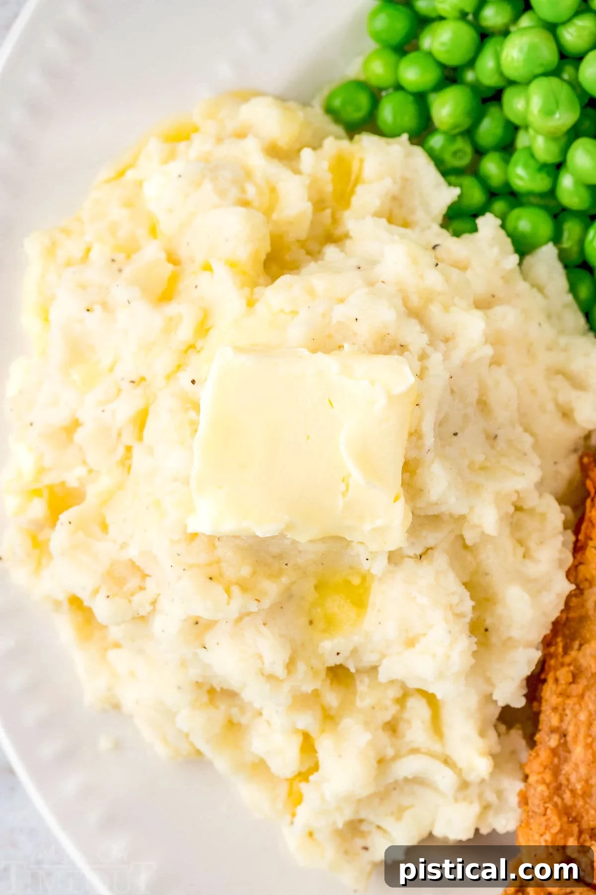 A perfectly portioned serving of Instant Pot Mashed Potatoes on a white dinner plate, accompanied by tender green peas and a succulent piece of chicken, creating a balanced and comforting meal.