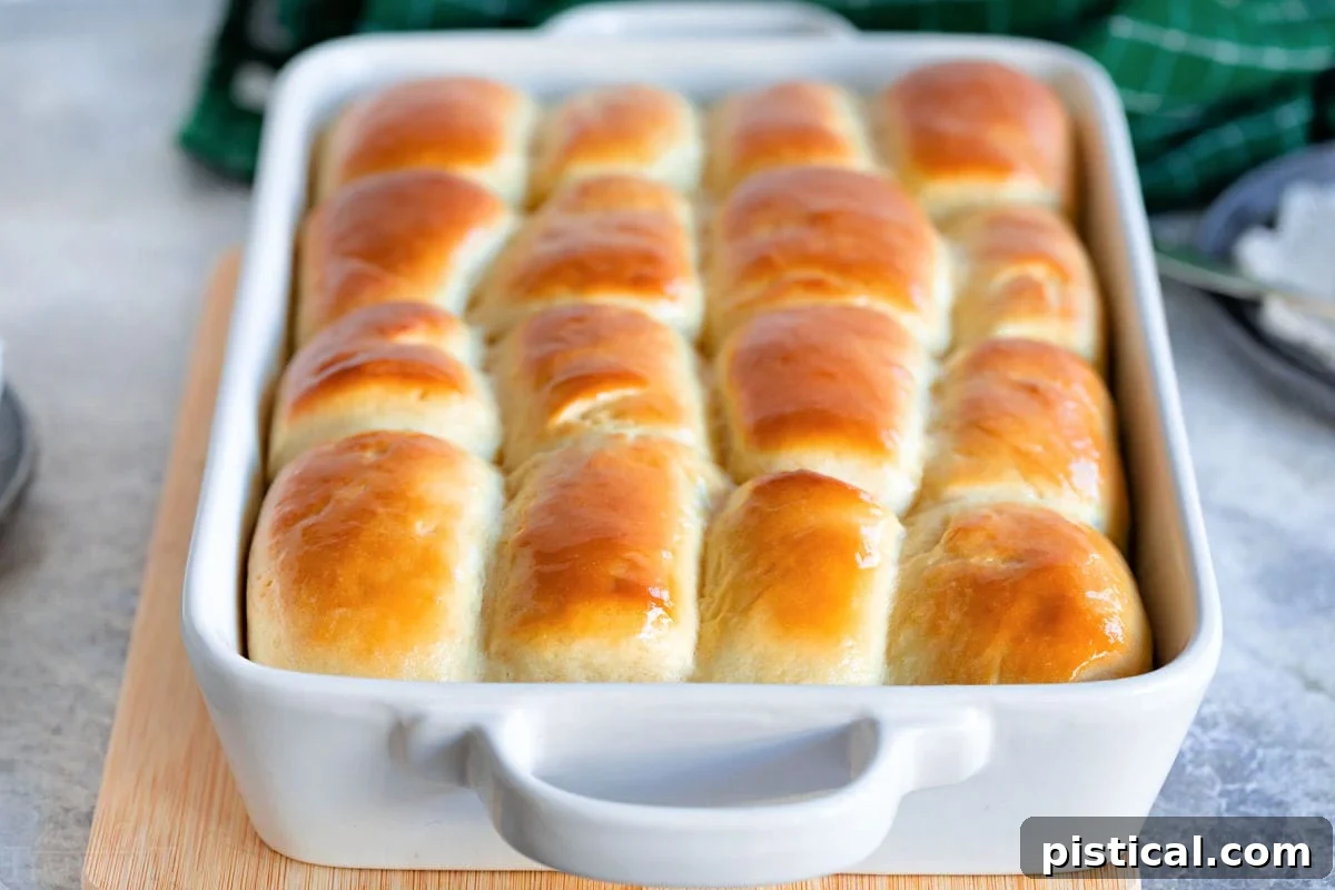 white baking dish with golden brown parker house rolls ready to be enjoyed. baking dish is sitting on cutting board.