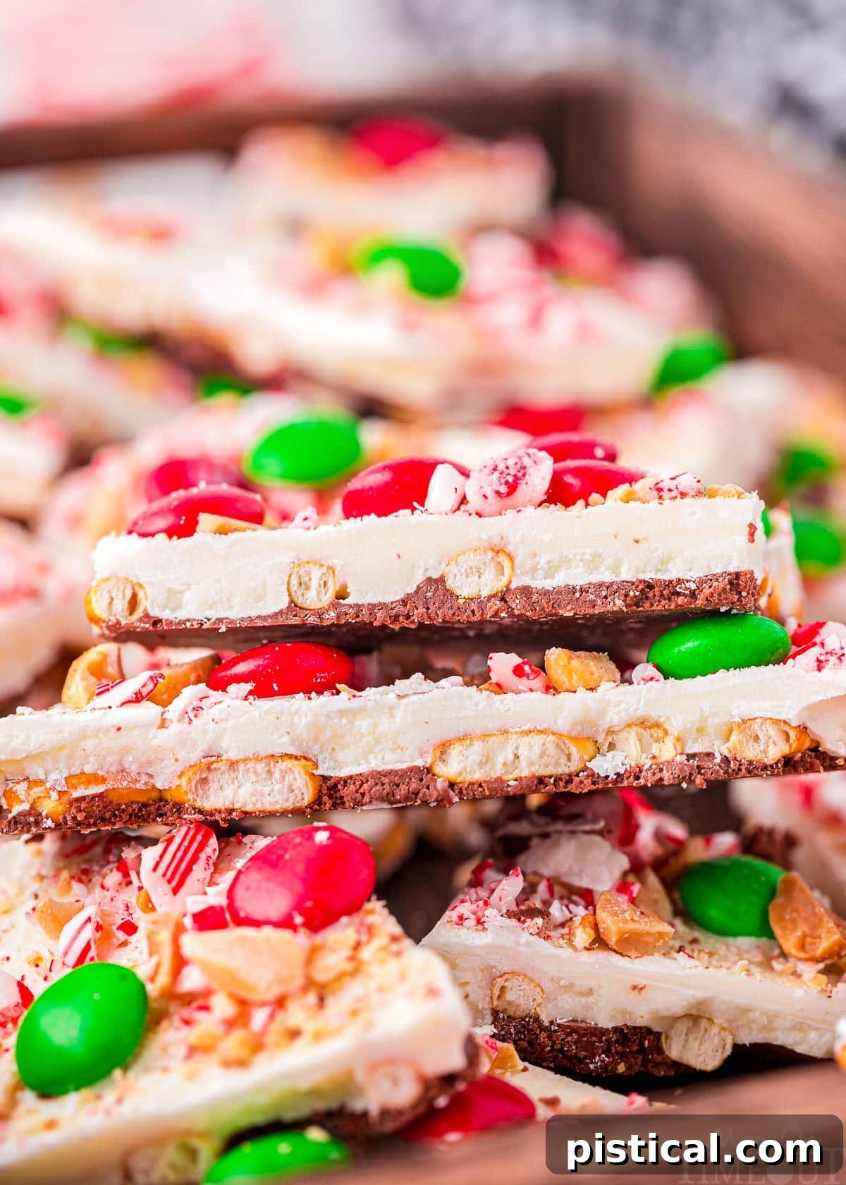 top down look at pieces of chocolate bark layered in a shallow wood tray. bark is decorated for christmas.